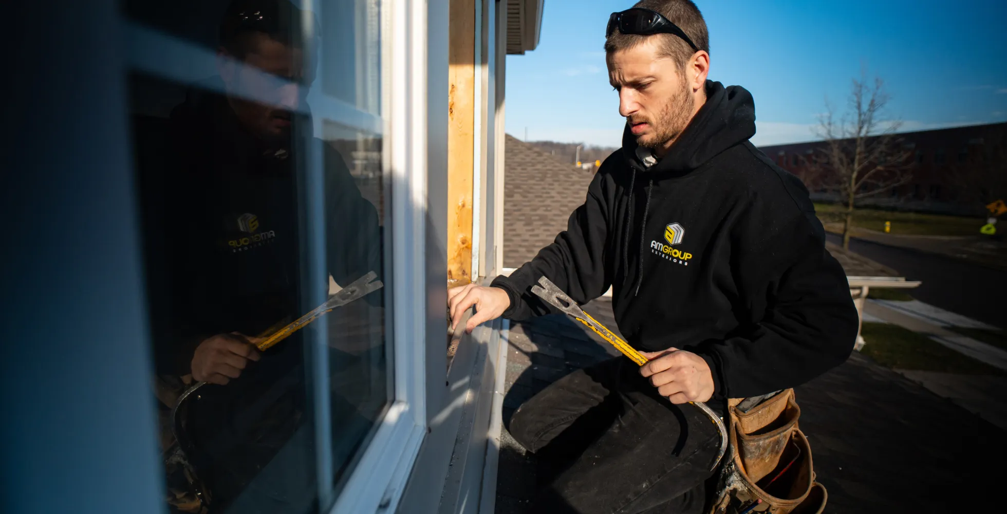 An AMGroup Exterior empoyee fixing a window while sitting on a roof